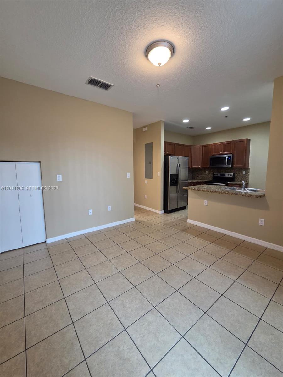 An open-concept kitchen with wood cabinets and tile flooring connects to a living area — 2851 W Prospect Rd # 404, Tamarac FL 33309, TAMARAC, FL