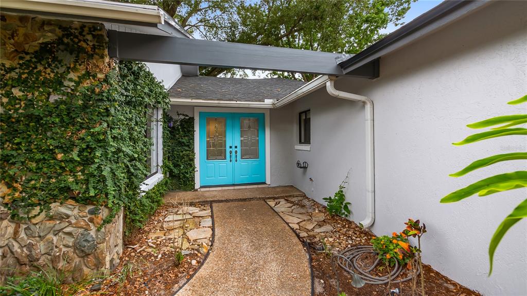 A stone-clad wall with climbing vines leads to a bright blue double front door — 901 CUTLER ROAD, LONGWOOD, FL