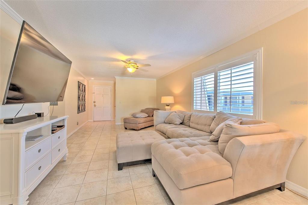 A living room features a large sectional sofa, a television on a white console, and tile flooring — 1008 APOLLO BEACH BOULEVARD UNIT 201, APOLLO BEACH, FL
