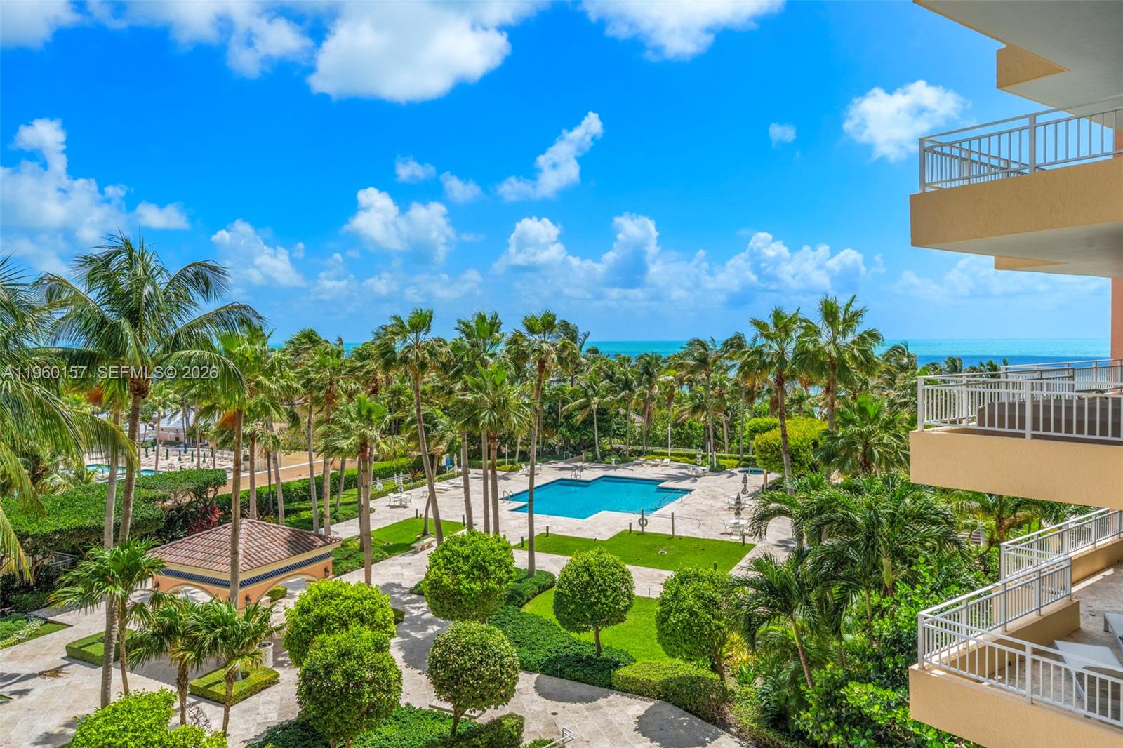 An elevated view of a swimming pool surrounded by palm trees and a coastal horizon — 799 Crandon Blvd # 605, Key Biscayne FL 33149, KEY BISCAYNE, FL