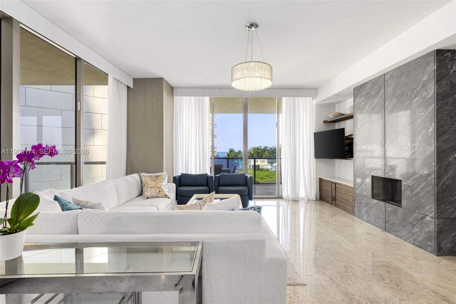 A modern living room features a white sectional sofa, blue armchairs, and a marble fireplace — 9701 Collins Ave # 404S, Bal Harbour FL 33154, BAL HARBOUR, FL