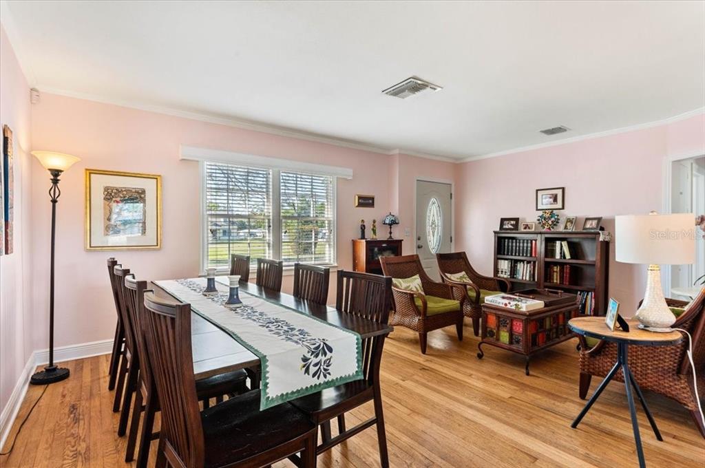 A dining and living area features light pink walls, hardwood floors, and wicker furniture — 2514 15TH AVENUE W, BRADENTON, FL