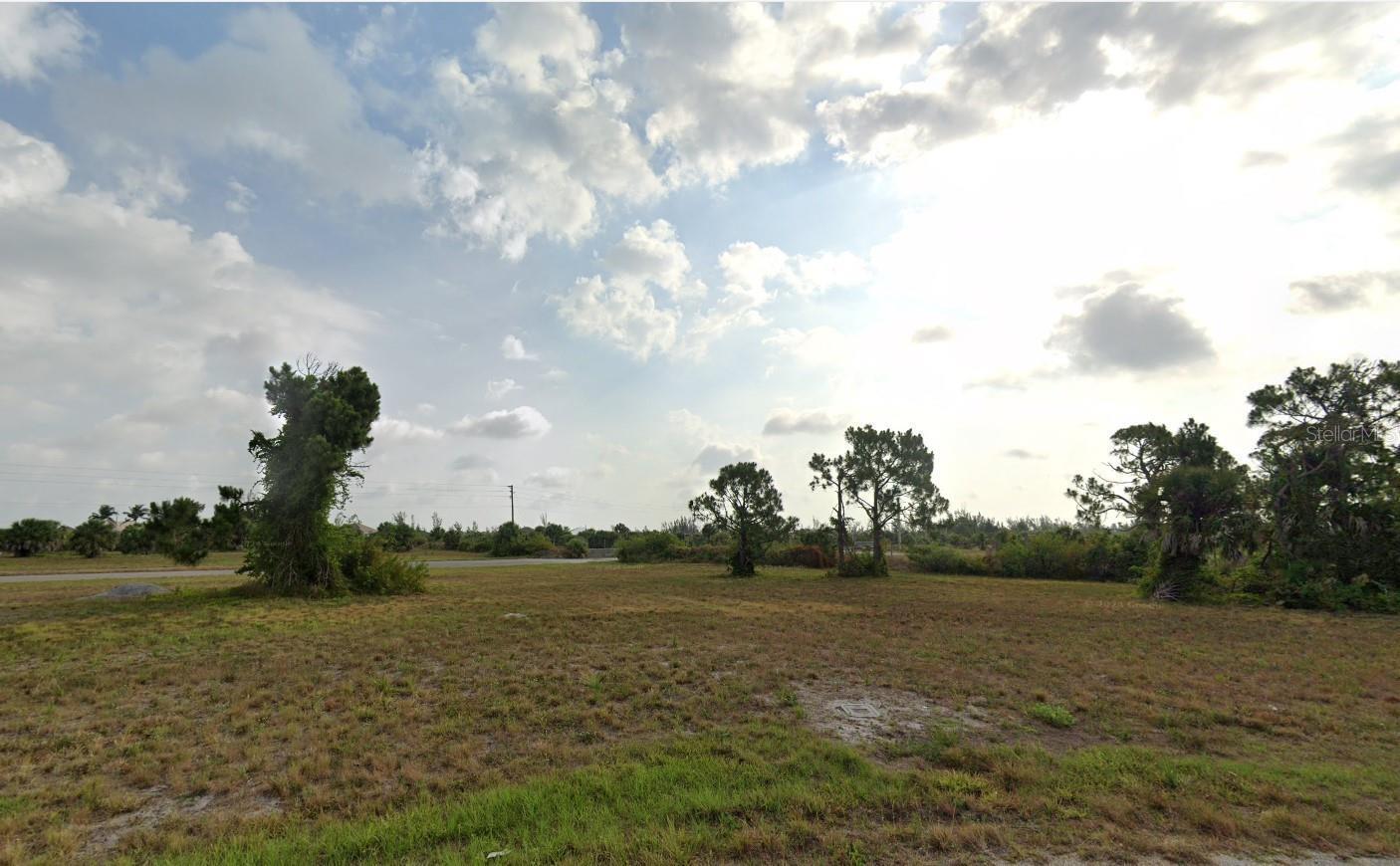 A vacant, grassy lot with scattered trees under a cloudy sky — 18 Satinwood Place, FL 33946, FL