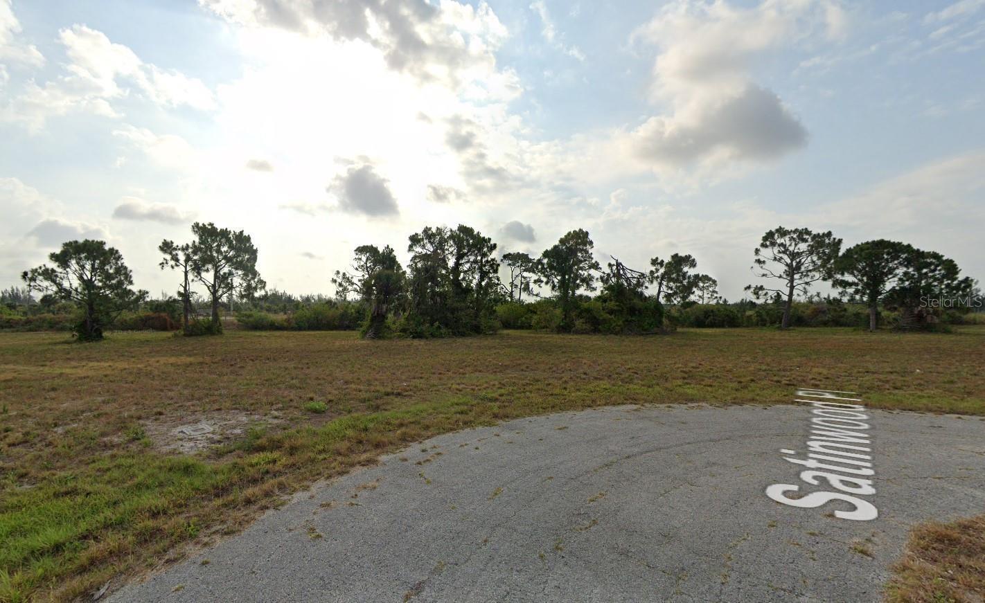 A paved cul-de-sac leads to a large, grassy vacant lot with scattered trees — 18 Satinwood Place, FL 33946, FL