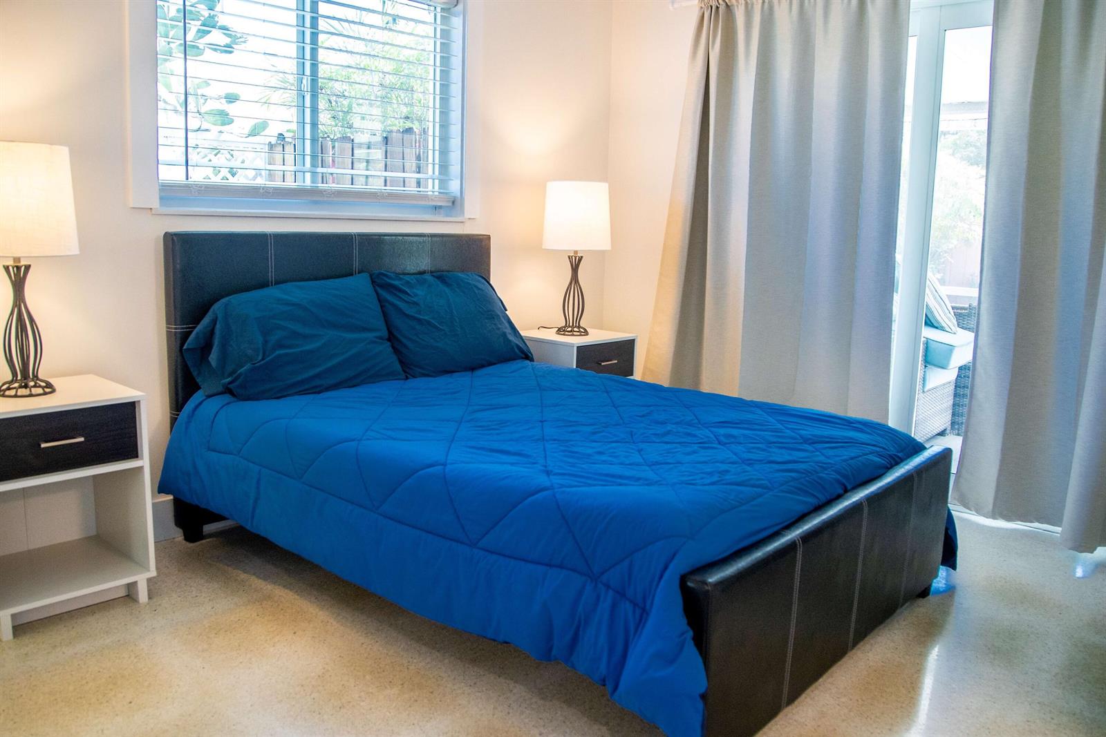 A bedroom features a bed with a blue quilt, two nightstands with lamps, and curtains — 22 Van Road, Jupiter FL 33469, JUPITER, FL