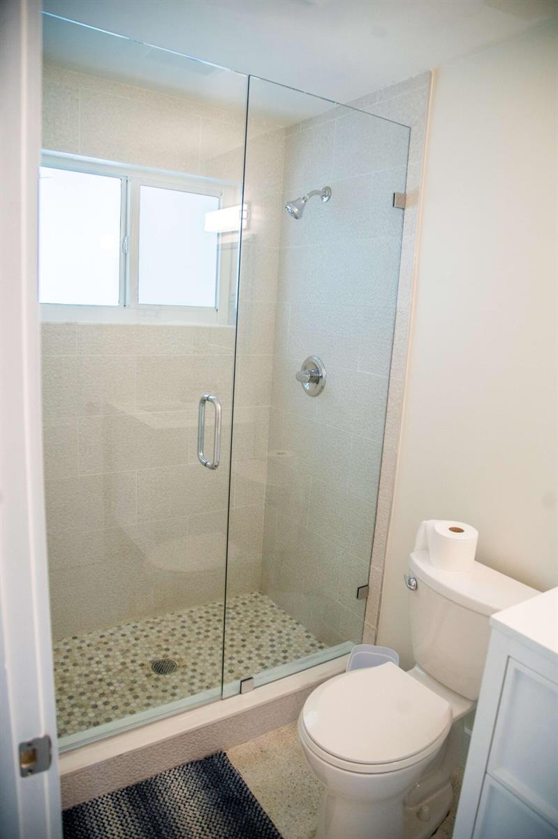 A bathroom features a glass-enclosed walk-in shower with pebble tile flooring and a white toilet — 22 Van Road, Jupiter FL 33469, JUPITER, FL