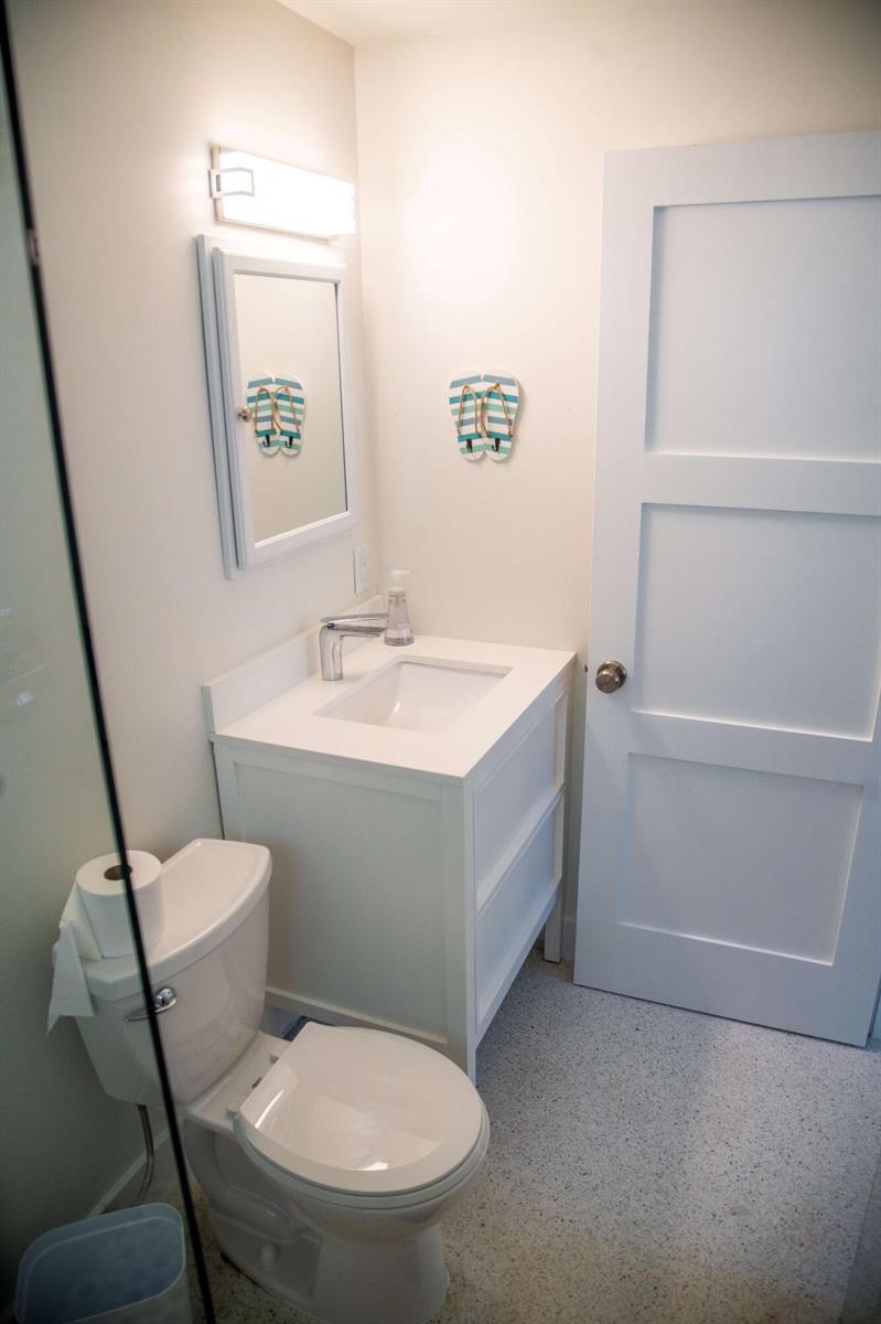 A small bathroom features a white vanity, a toilet, and a mirror with flip-flop decor — 22 Van Road, Jupiter FL 33469, JUPITER, FL