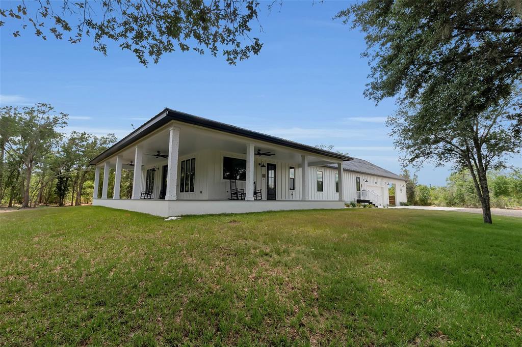 A white farmhouse with a large wrap-around porch sits on a grassy lot with trees — 40916 11TH AVENUE EAST, MYAKKA CITY, FL