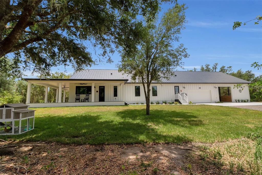 A white farmhouse with a metal roof, front porch, and attached garage sits on grass — 40916 11TH AVENUE EAST, MYAKKA CITY, FL