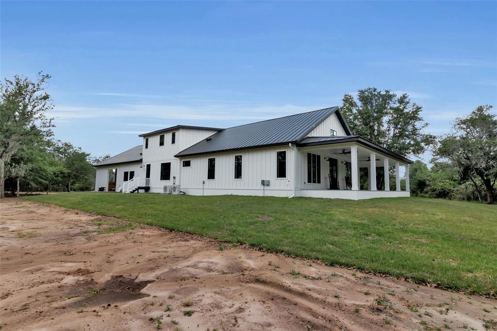 A white farmhouse with a black metal roof and a covered porch sits on grass — 40916 11TH AVENUE EAST, MYAKKA CITY, FL