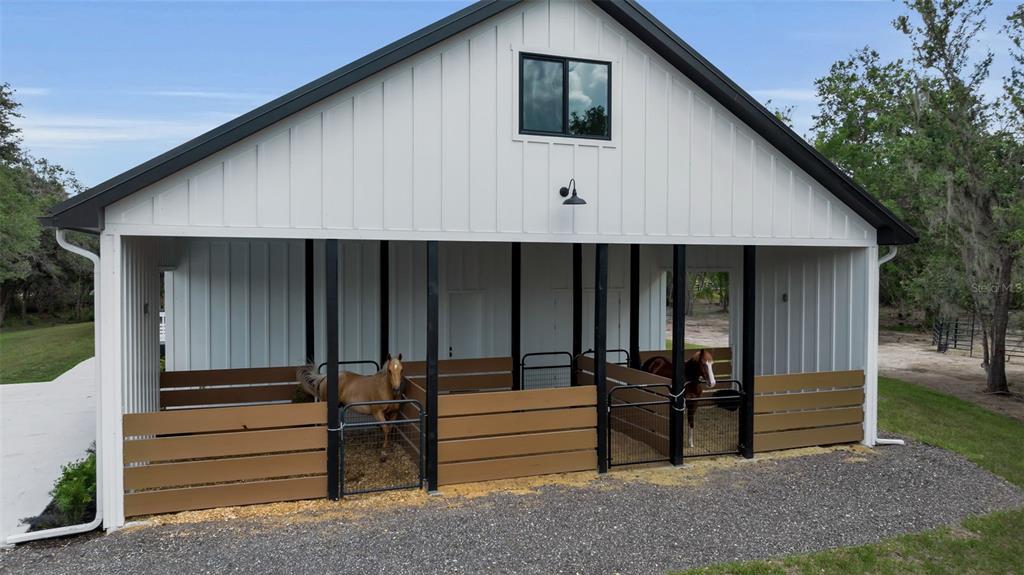 A white barn with a black roof features two open horse stalls with brown fencing — 40916 11TH AVENUE EAST, MYAKKA CITY, FL