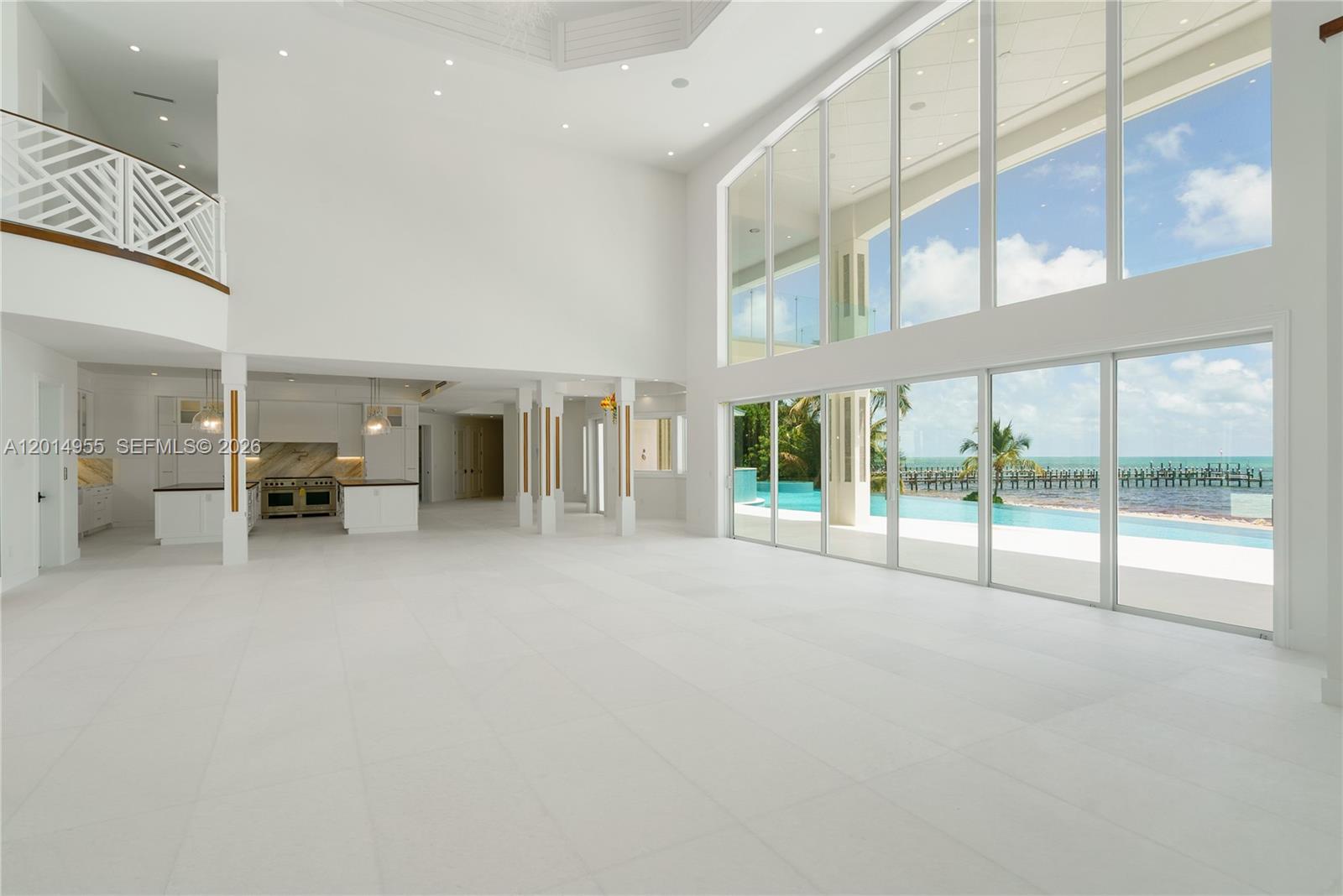 A spacious, white-tiled living area features double-height ceilings, floor-to-ceiling windows, and a view of a pool — 88845 Old Hwy, Tavernier FL 33070, TAVERNIER, FL