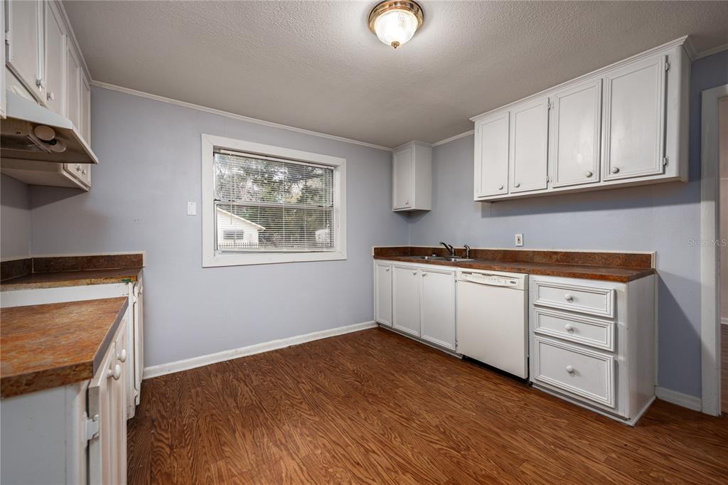 A kitchen features white cabinets, brown laminate countertops, light blue walls, and wood-look flooring — 1001 NE 2ND AVENUE, TRENTON, FL