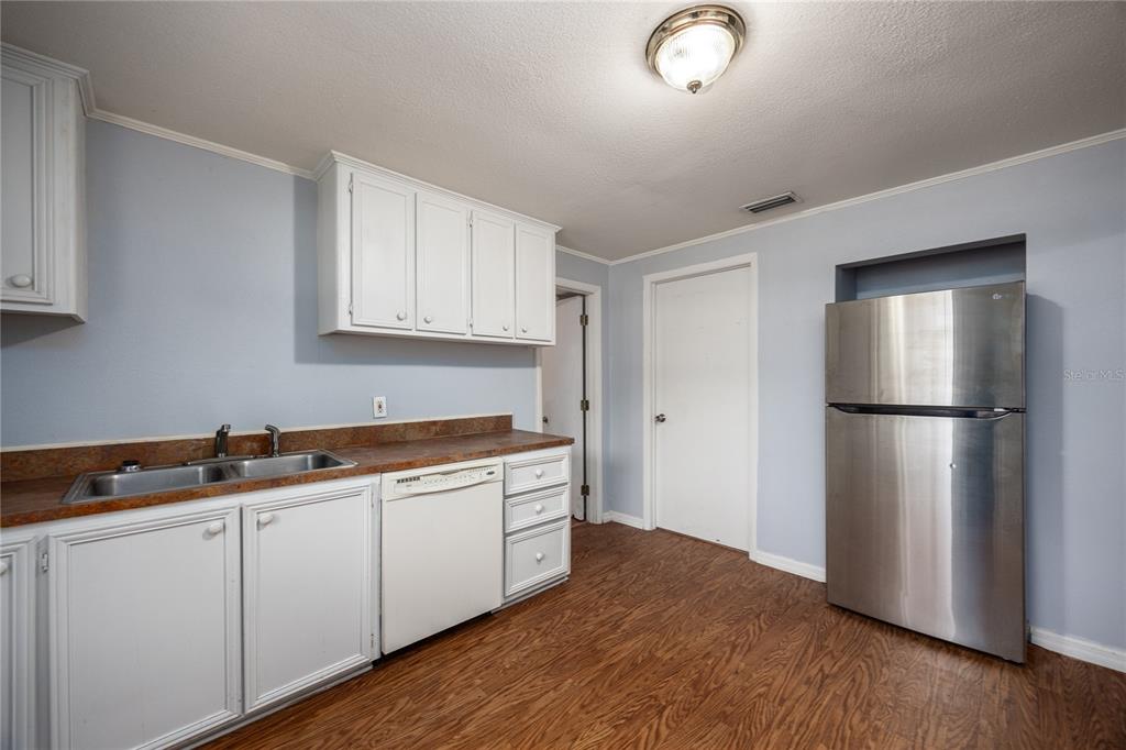 A kitchen features white cabinets, a stainless steel refrigerator, a dishwasher, and wood-look flooring — 1001 NE 2ND AVENUE, TRENTON, FL