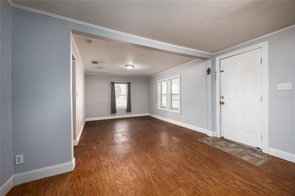 An empty living room features light blue walls, wood-look flooring, and a white front door — 1001 NE 2ND AVENUE, TRENTON, FL
