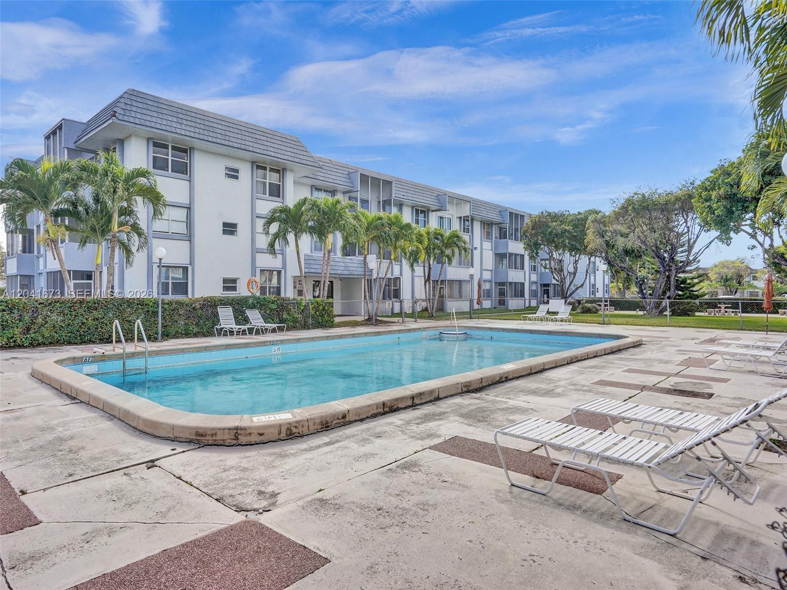 A rectangular swimming pool sits on a concrete deck in front of a multi-story building — 6705 NW 169th St # C112, Hialeah FL 33015, HIALEAH, FL