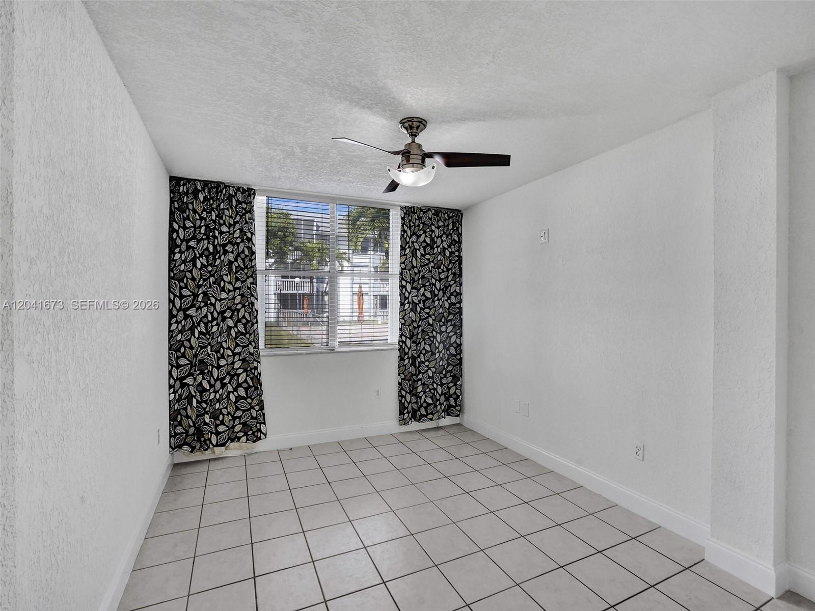 A room with white walls, tiled flooring, a ceiling fan, and patterned curtains over windows — 6705 NW 169th St # C112, Hialeah FL 33015, HIALEAH, FL