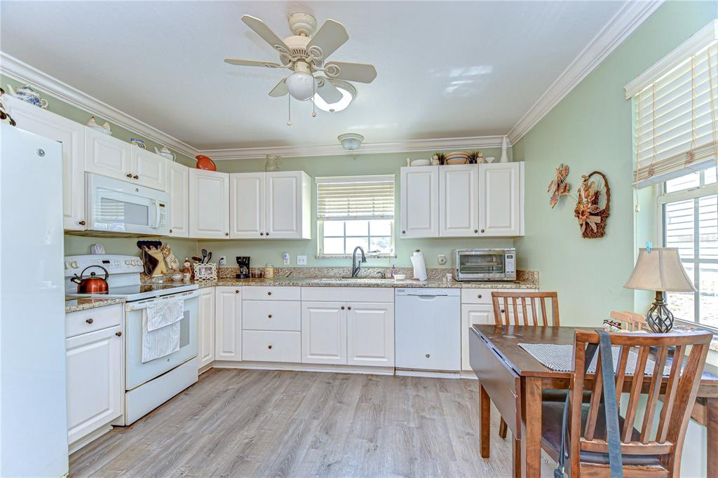 A kitchen with white cabinets, granite countertops, light green walls, and a wooden dining table — 5906 GREENBRIAR COURT, ZEPHYRHILLS, FL