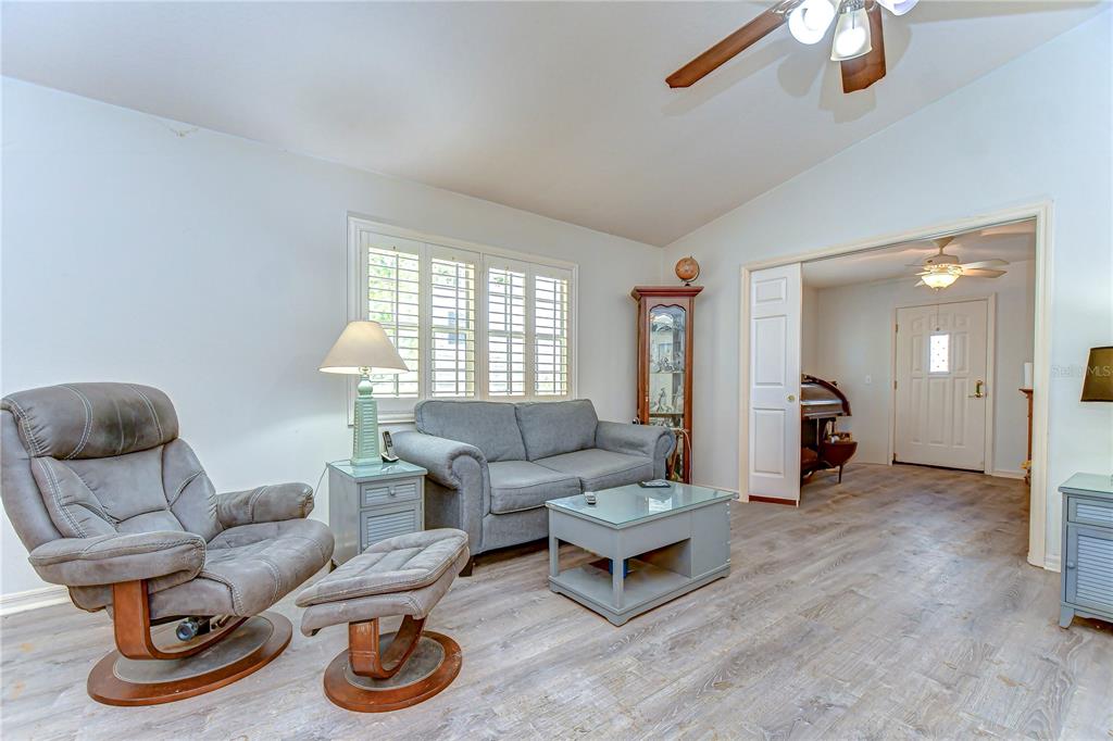 A living room features a gray sofa, a matching recliner with ottoman, and wood-look flooring — 5906 GREENBRIAR COURT, ZEPHYRHILLS, FL