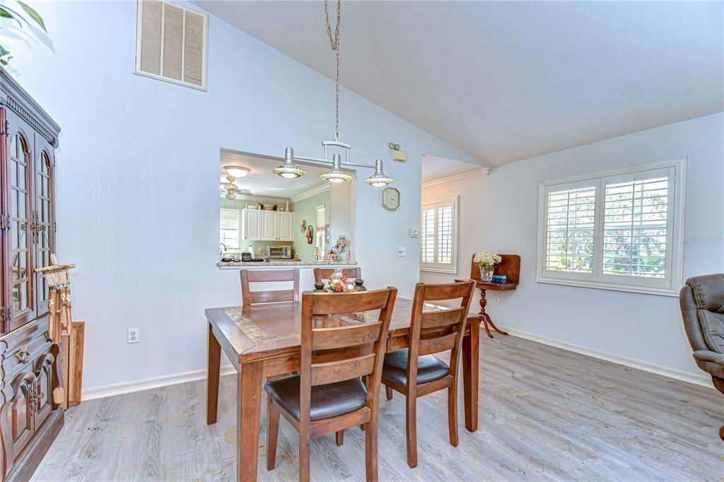 A dining room with a wooden table, chairs, light-colored flooring, and a kitchen pass-through window — 5906 GREENBRIAR COURT, ZEPHYRHILLS, FL