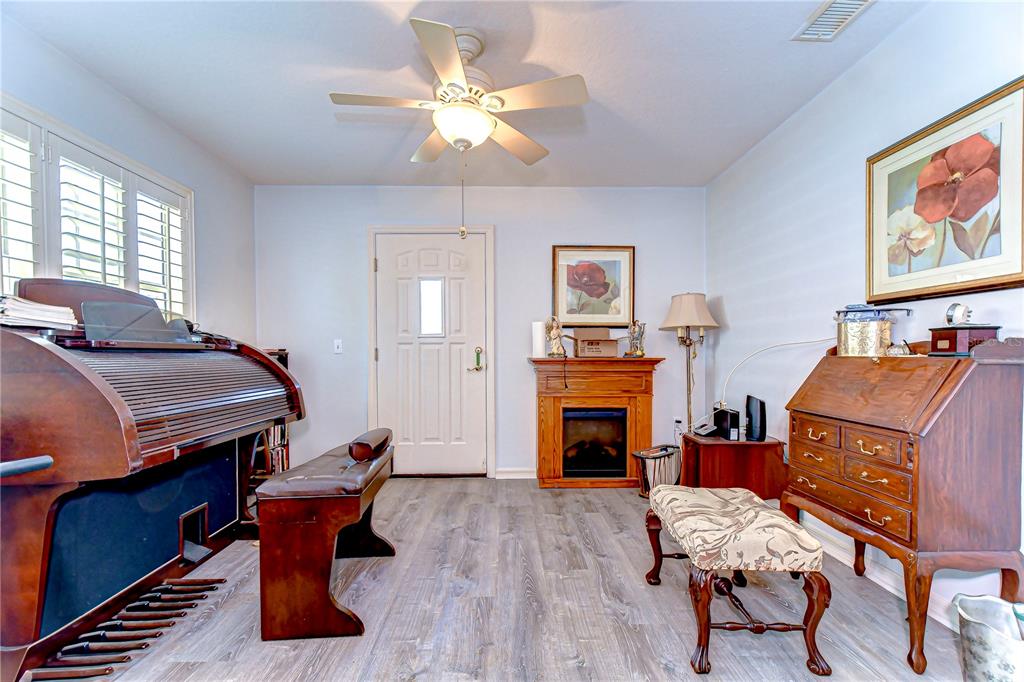 A room with wood-look flooring features a piano, a fireplace, and a wooden secretary desk — 5906 GREENBRIAR COURT, ZEPHYRHILLS, FL