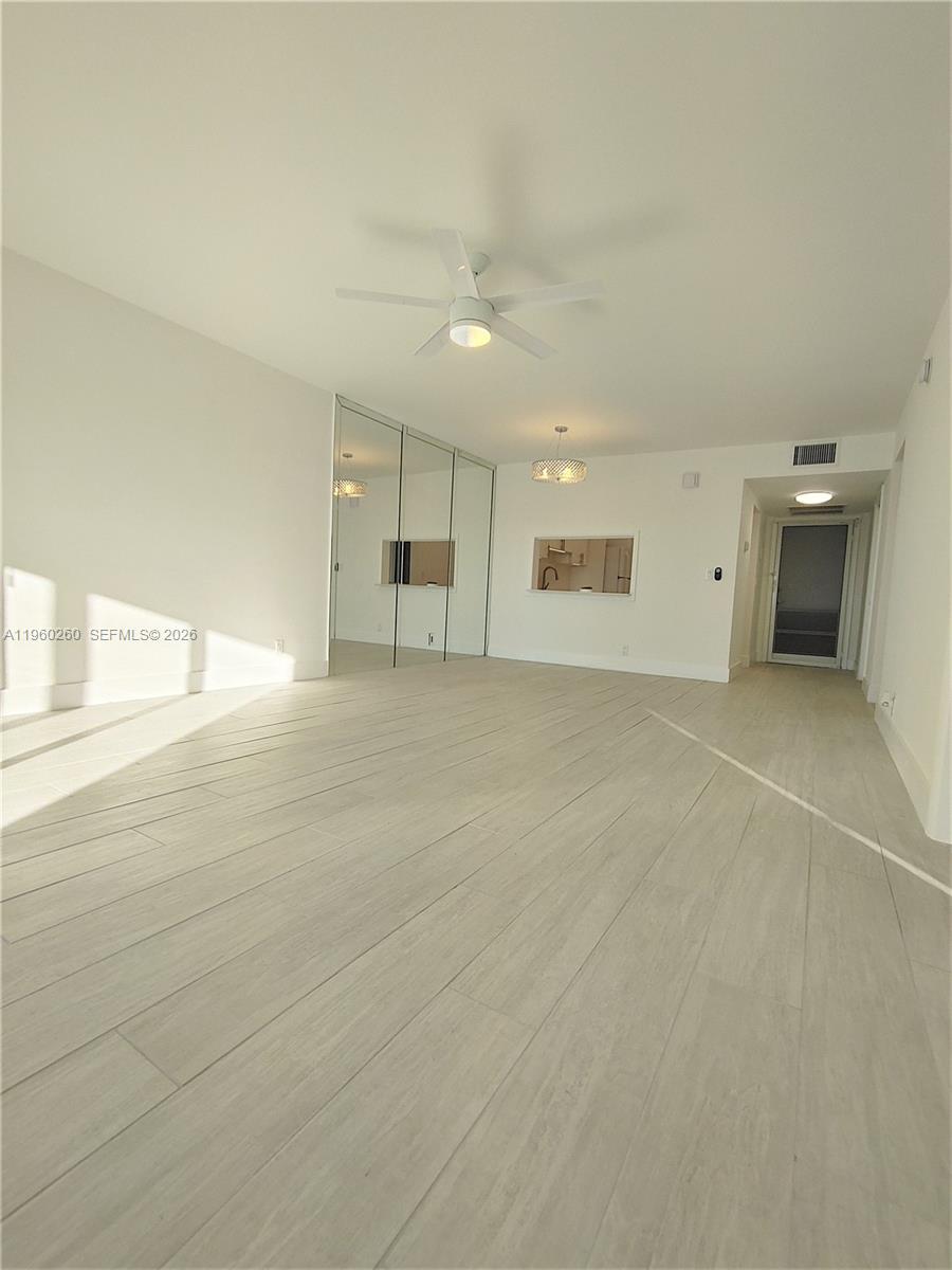 A bright, empty room features light wood-look flooring, a ceiling fan, and mirrored closet doors — 215 SE 3rd Ave # 307C, Hallandale Beach FL 33009, HALLANDALE BEACH, FL