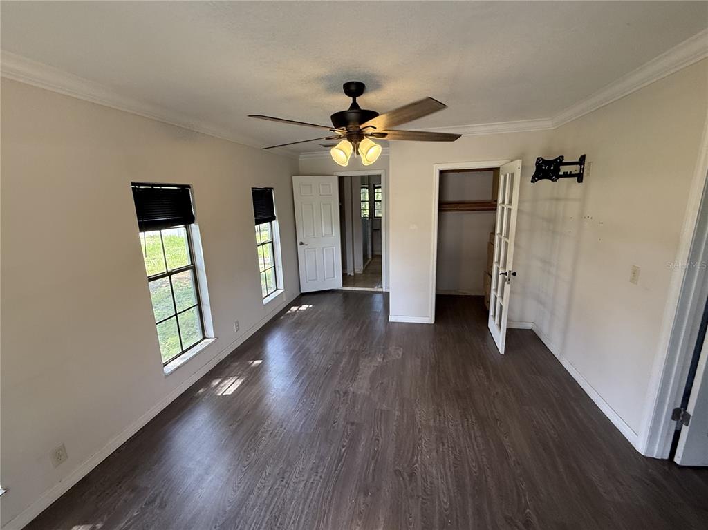 A room with dark wood-look flooring, two windows, a ceiling fan, and two open doorways — 205 TRACY WAY, LAKELAND, FL