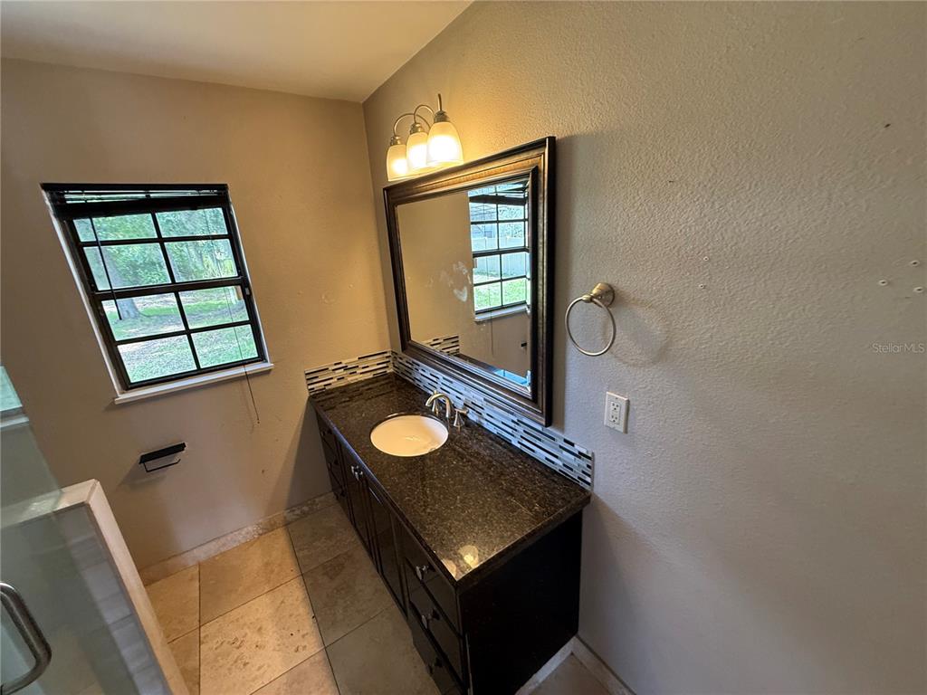 A bathroom features a dark wood vanity with a granite countertop, mirror, and window — 205 TRACY WAY, LAKELAND, FL