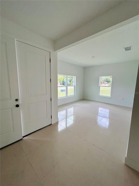 An empty room with white walls, tiled floors, and two windows near an entrance door — 239 GREENBRIER AVENUE NW, PALM BAY, FL
