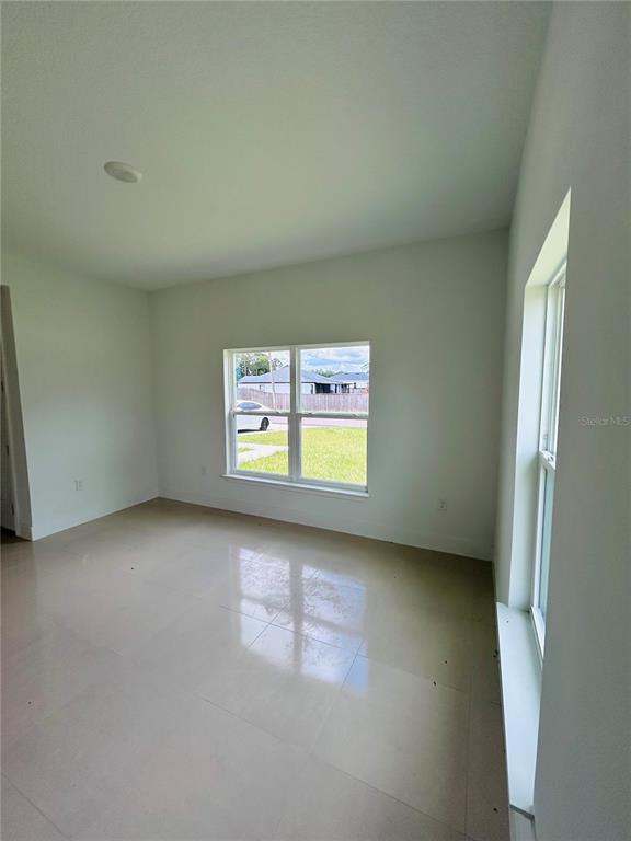 An empty room with light-colored tile flooring, white walls, and two windows — 239 GREENBRIER AVENUE NW, PALM BAY, FL