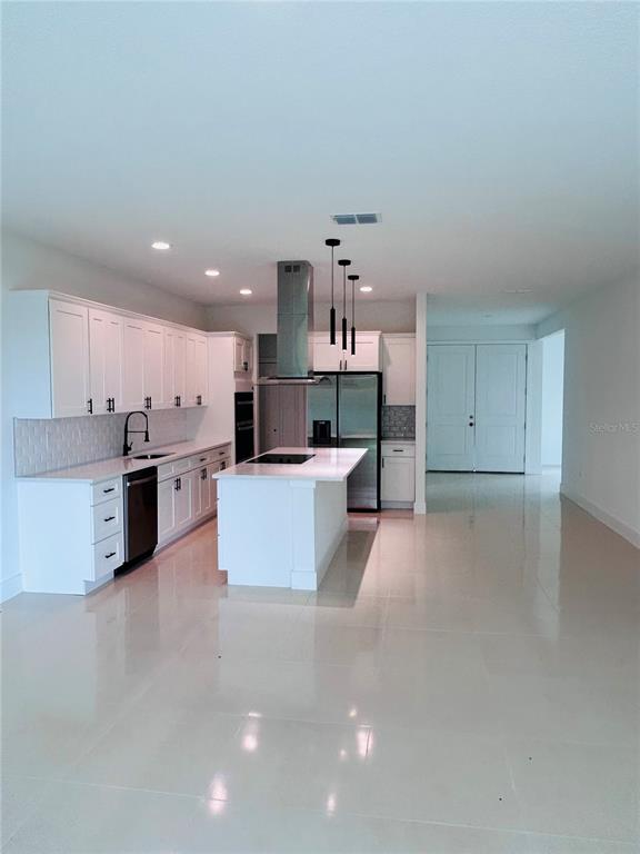A modern white kitchen features a central island, stainless steel appliances, and glossy tile floors — 239 GREENBRIER AVENUE NW, PALM BAY, FL