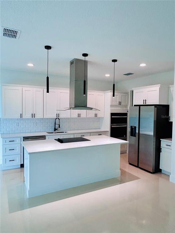 A modern kitchen features white cabinetry, a central island with a cooktop, and stainless appliances — 239 GREENBRIER AVENUE NW, PALM BAY, FL