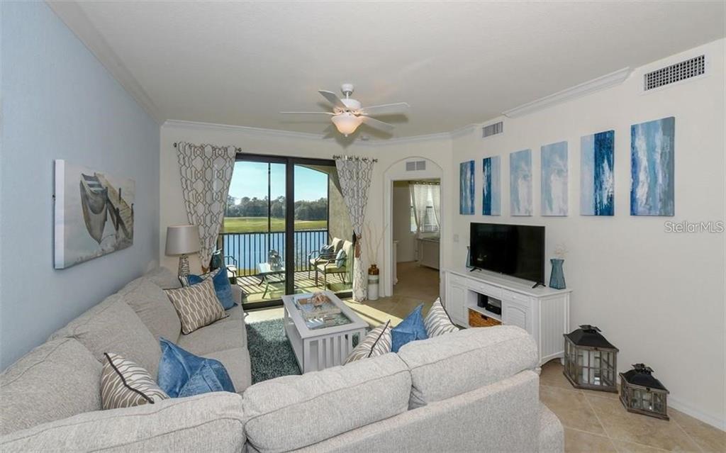 A living room features a sectional sofa, a television, and a balcony overlooking a lake — 16904 VARDON TERRACE UNIT 201, LAKEWOOD RANCH, FL