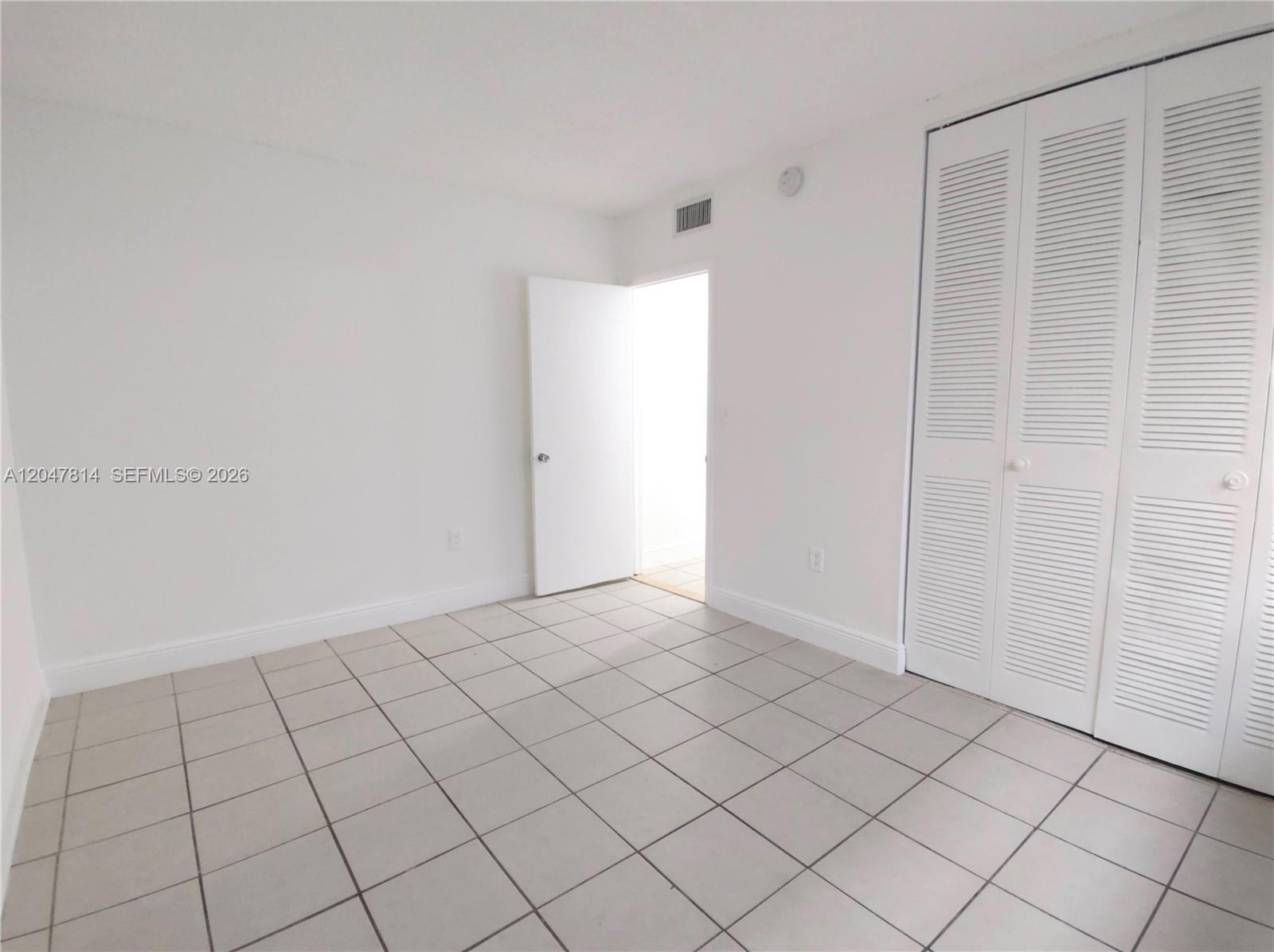 An empty room features white walls, light-colored floor tiles, and white louvered closet doors — 1265 W 24th St # 108, Hialeah FL 33010, HIALEAH, FL