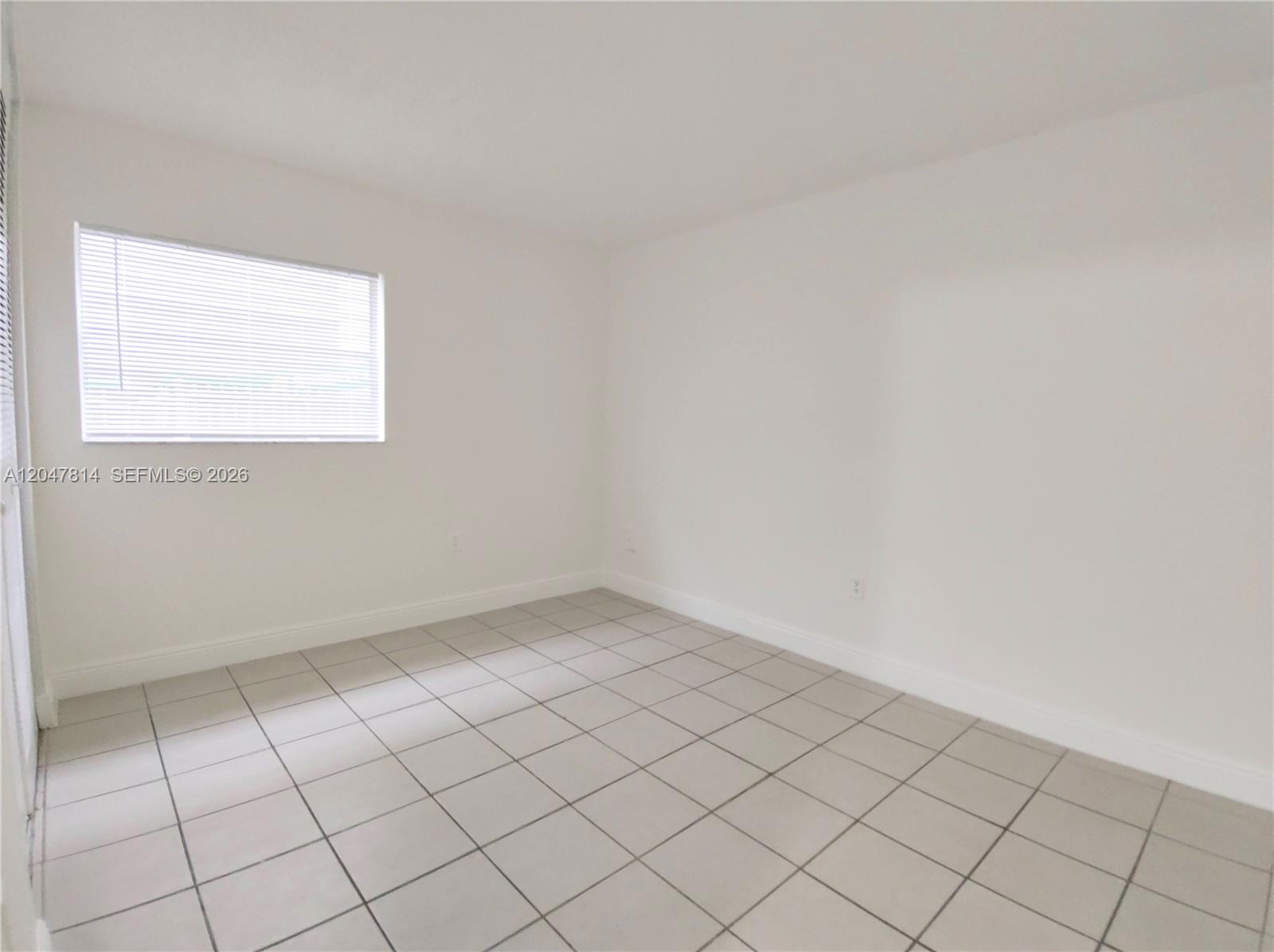 An empty room features white walls, a single window with blinds, and light-colored tiled flooring — 1265 W 24th St # 108, Hialeah FL 33010, HIALEAH, FL