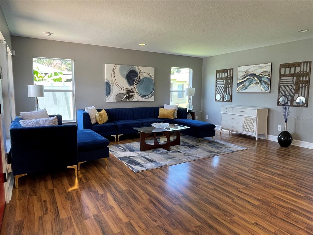 A living room features a blue sectional sofa, a glass coffee table, and wood flooring — 5036 WHISTLING PINES COURT, WESLEY CHAPEL, FL