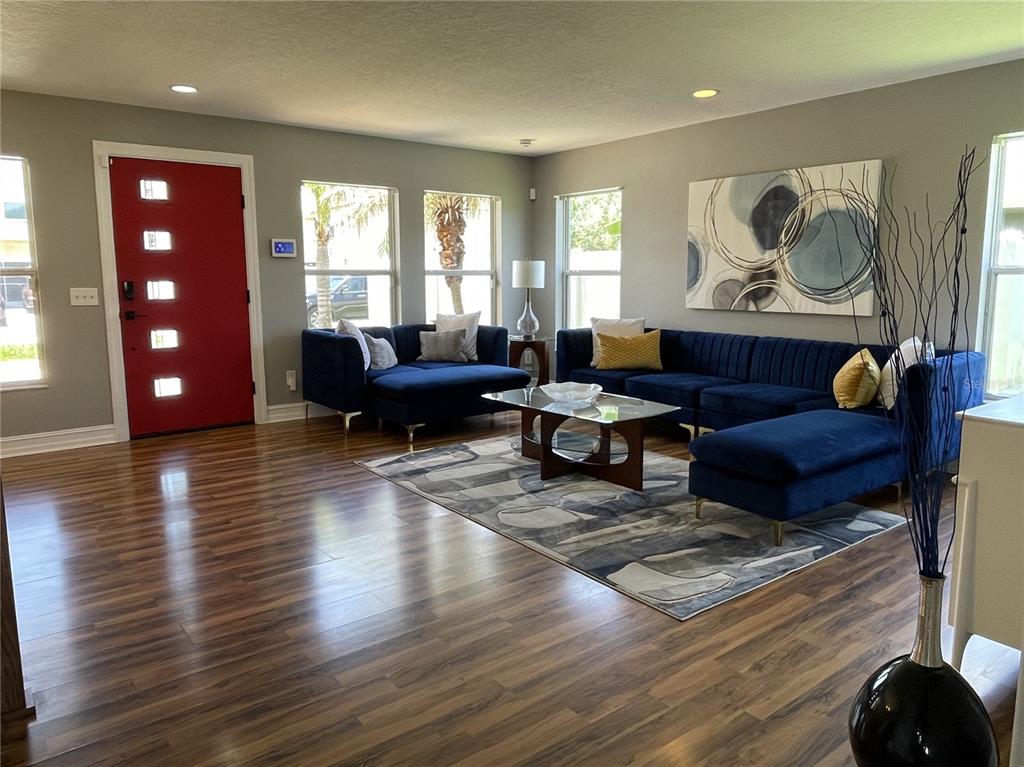A living room features dark blue sectionals, a glass coffee table, and a red front door — 5036 WHISTLING PINES COURT, WESLEY CHAPEL, FL