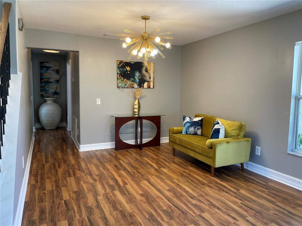 A room with wood-look flooring, a green velvet loveseat, a glass console table, and chandelier — 5036 WHISTLING PINES COURT, WESLEY CHAPEL, FL