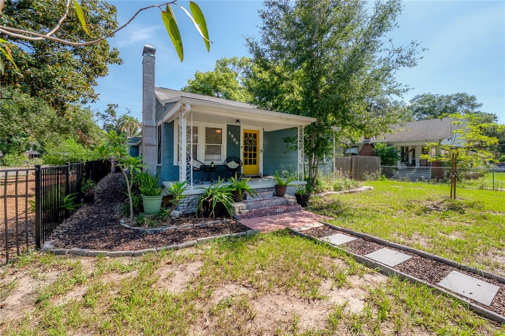 A blue cottage with a yellow front door and a covered porch sits on a lawn — 1300 E HENRY AVENUE, TAMPA, FL