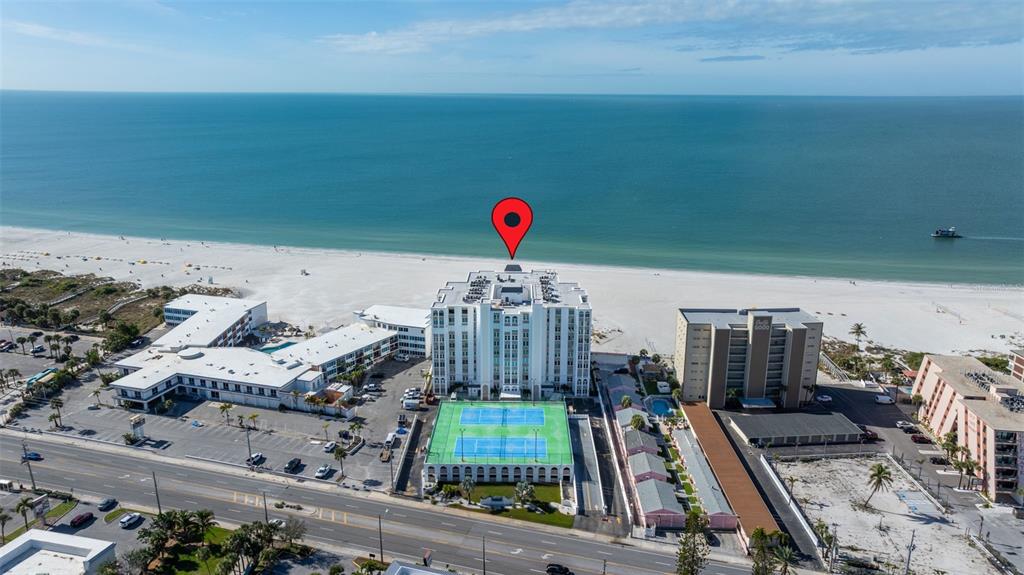 An aerial view of a beach with several multi-story buildings and a small pink house — 4950 GULF BOULEVARD UNIT 207, ST PETE BEACH, FL