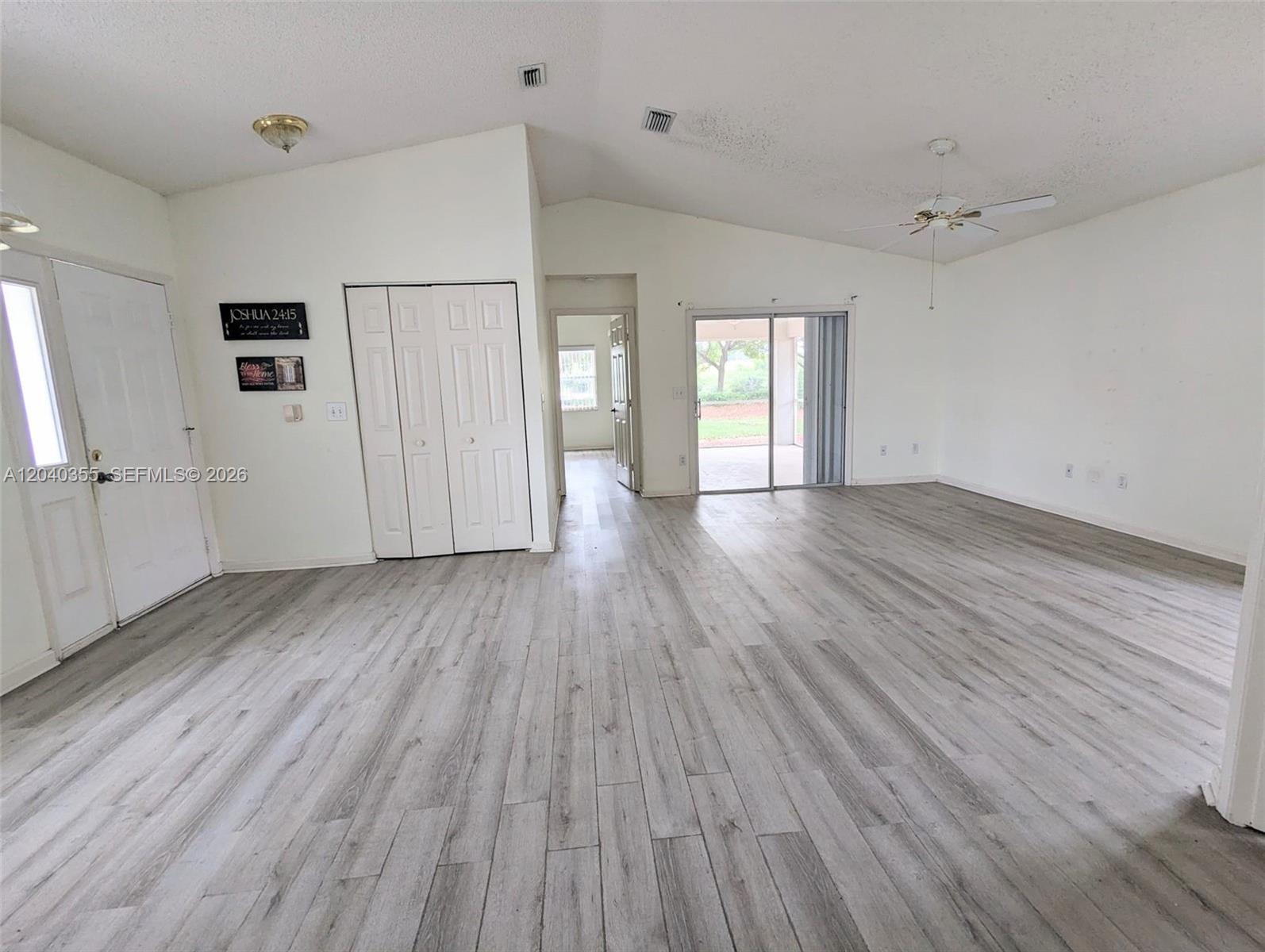 A living room features vaulted ceilings, light wood-look flooring, white walls, and a sliding glass door — 532 SE 21st Dr, Homestead FL 33033, HOMESTEAD, FL