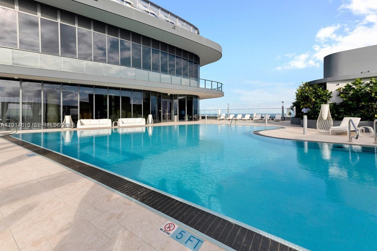 A modern building features a large swimming pool with lounge chairs on a rooftop terrace — 1000 Brickell Plz # 2101, Miami FL 33131, MIAMI, FL