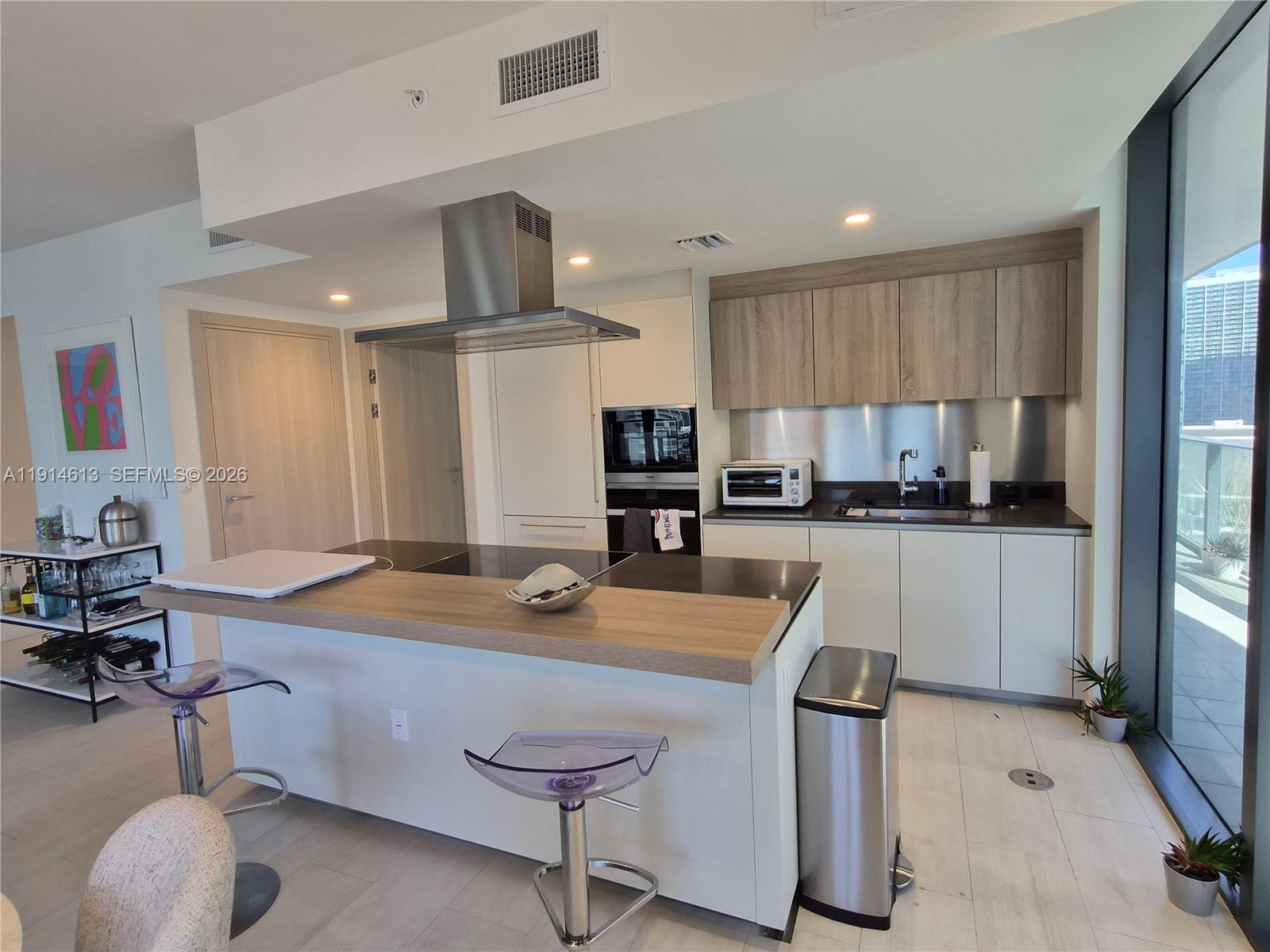 A modern kitchen features a central island, stainless steel appliances, and light wood cabinetry — 1000 Brickell Plz # 2101, Miami FL 33131, MIAMI, FL