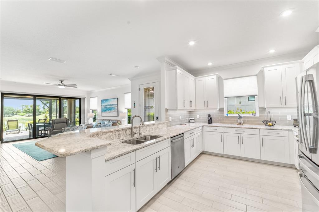 A kitchen with white cabinets, granite countertops, and stainless steel appliances overlooks a living area — 5362 CICERONE STREET, SARASOTA, FL