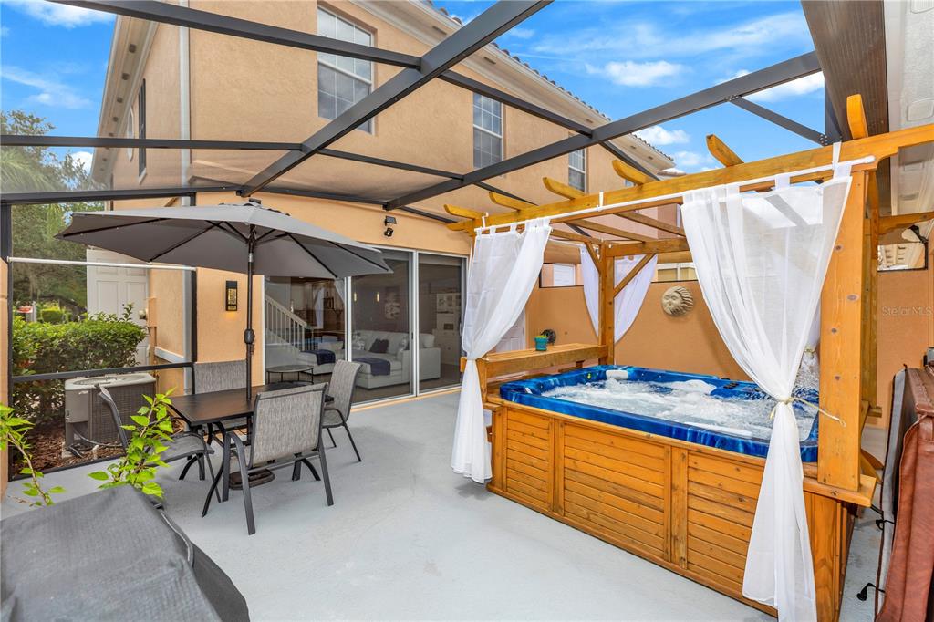 A screened-in patio features a dining set, a hot tub with a wooden pergola, and curtains — 8418 LEATHERLEAF LANE, ORLANDO, FL
