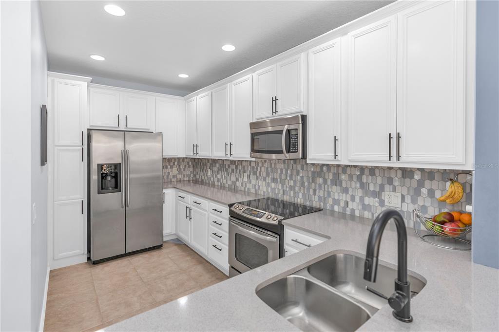 A kitchen features white cabinetry, stainless steel appliances, a gray backsplash, and a double sink — 8418 LEATHERLEAF LANE, ORLANDO, FL