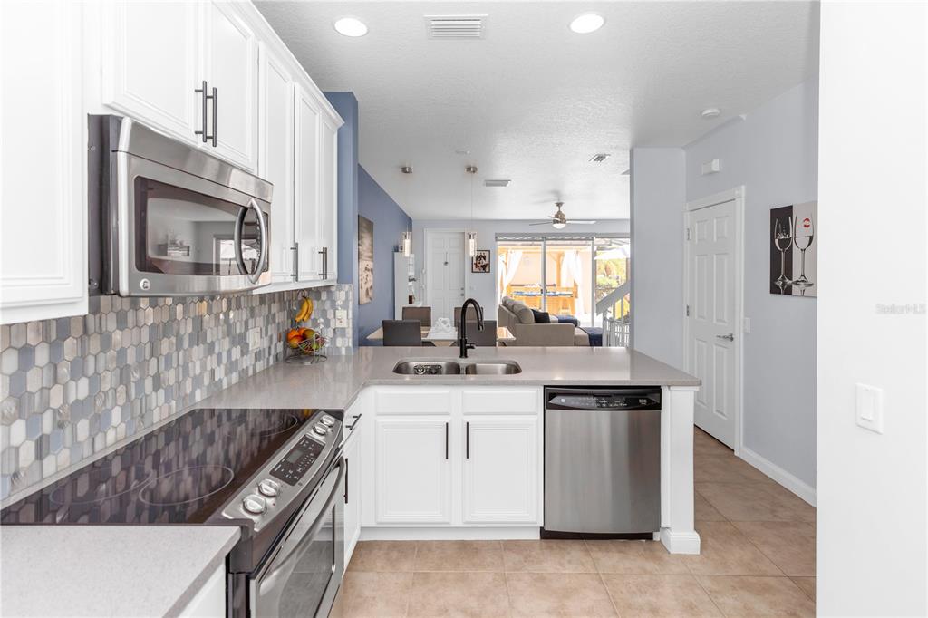A kitchen with white cabinets, stainless steel appliances, and a gray countertop overlooks a living area — 8418 LEATHERLEAF LANE, ORLANDO, FL