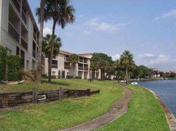 A multi-story apartment building sits along a grassy waterfront with a paved walking path — 6319 NEWTOWN CIRCLE UNIT 19B6, TAMPA, FL