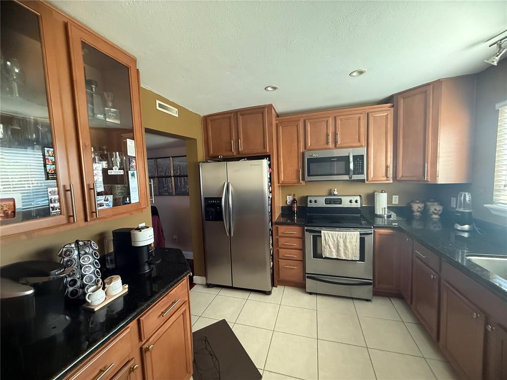 A kitchen features wood cabinets, stainless steel appliances, black countertops, and light-colored tile flooring — 6319 NEWTOWN CIRCLE UNIT 19B6, TAMPA, FL