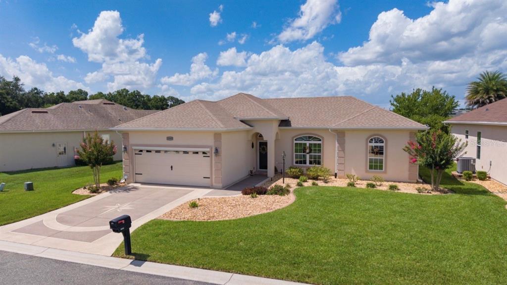 A single-story suburban house with a tan stucco exterior, a two-car garage, and a lawn — 10949 SE 169TH LANE, SUMMERFIELD, FL